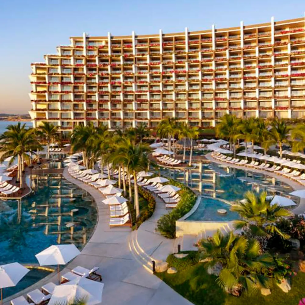 A luxury beachfront resort in Los Cabos with tiered pools, palm-lined terraces, and lounge seating at golden hour